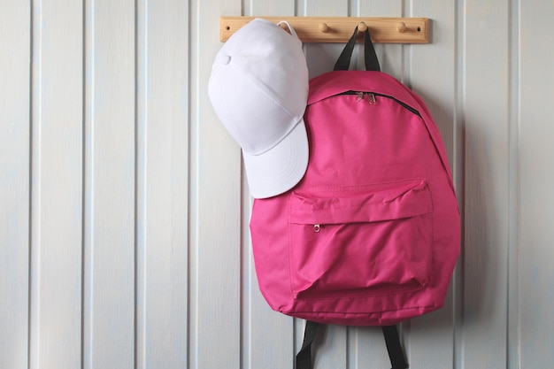 Mochila escolar rosa e um boné de beisebol branco estão pendurados em um cabide