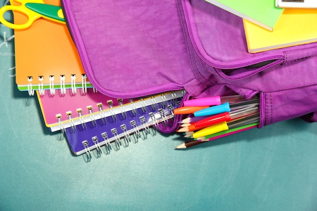 Foto mochila morada con útiles escolares sobre fondo de escritorio verde