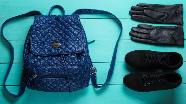 Mochila na moda couro, luvas, botas em uma superfície de madeira azul. Acessórios de tendência.