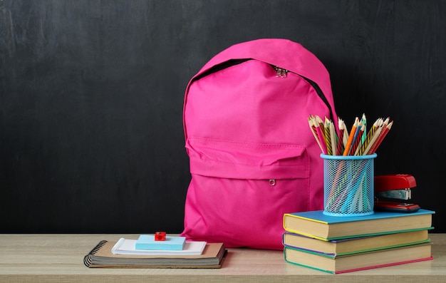 Mochila rosa e material escolar em cima da mesa em um fundo preto