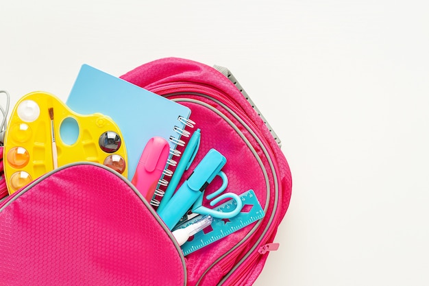 Mochila rosa con material escolar sobre fondo blanco. De vuelta a la escuela.