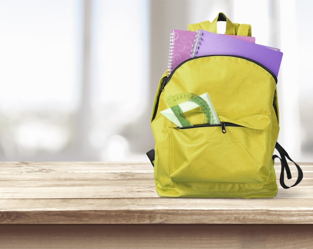 mochila con suministros escolares en la mesa sobre el interior educativo borroso