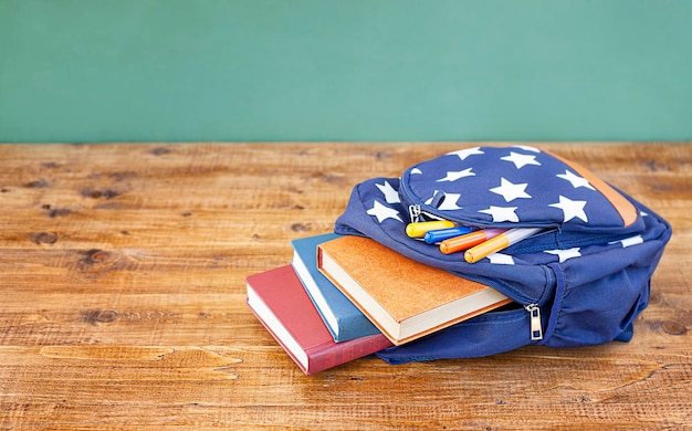 una mochila con útiles escolares se encuentra sobre una mesa de madera contra el fondo de una pizarra