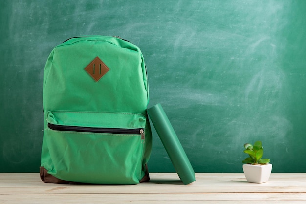 Mochila verde y libro en el fondo de la pizarra.