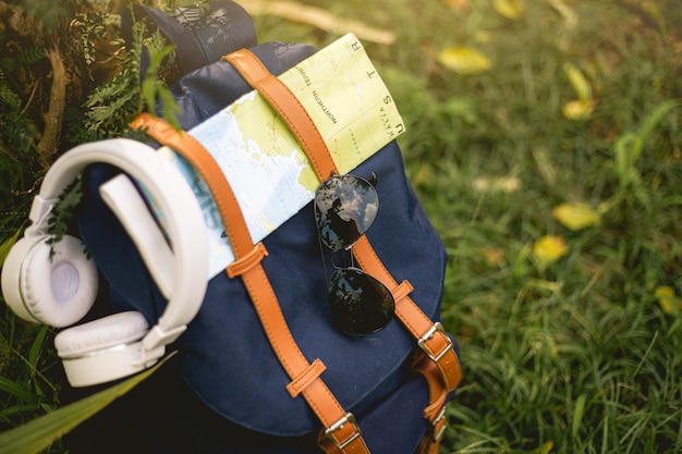 Mochila de viaje con sombrero, cámara, mapa, auriculares y teléfono inteligente en el parque