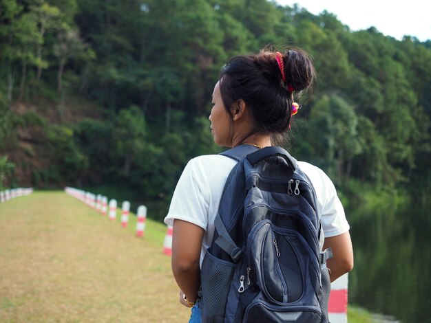 Mochila de viajero joven asiática de pie solo frente al bosque y el fondo de la laguna