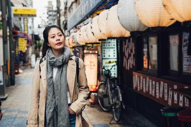 mochileiro de garota atraente andando pelas lanternas brancas penduradas no telhado do lado de fora do izakaya em shinsekai osaka japão. jovem no caminho em zona urbana tranquila pela manhã.