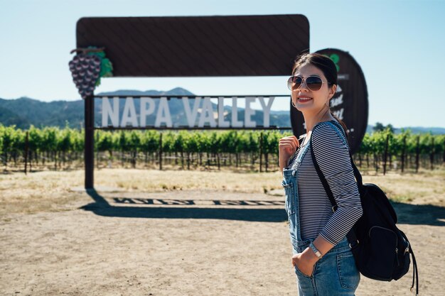 mochileiro de mulher asiática em pé na frente do vinhedo de napa valley posando tirando foto sob o sol enquanto as férias de verão viajam em san francisco america. jovem em óculos de sol rosto câmera sorriso.