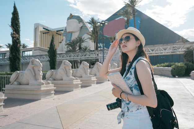 mochileiro de viagens elegante senhora desfrutar de pausas na cidade nas férias de verão. Vista lateral do fotógrafo de garota encantadora em óculos de sol com câmera e livro de guia de viajantes fica ao ar livre em dia ensolarado com Esfinge.