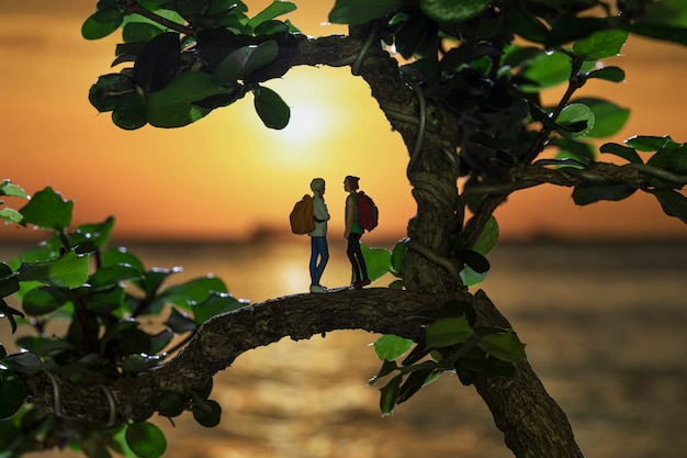 Foto mochileiro em miniatura ficar em árvores em um fundo do sol de silhueta.