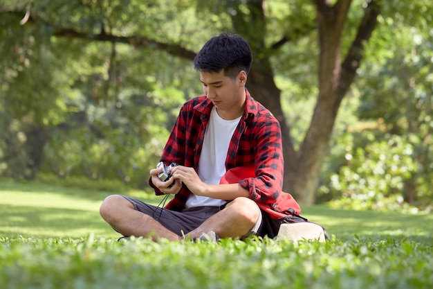 Mochileiro jovem asiático sentado no campo de grama em um dia de verão cara bonito desfrutar com estilo de vida ao ar livre nas férias de férias