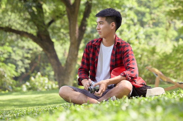 Mochileiro jovem asiático sentado no campo de grama em um dia de verão cara bonito desfrutar com estilo de vida ao ar livre nas férias de férias