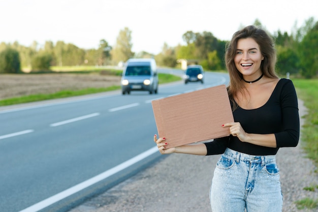 Mochileiro na estrada está segurando uma placa de papelão em branco