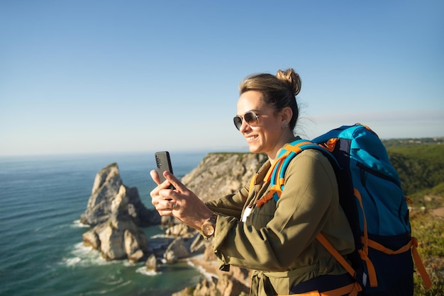 Mochilero mujer feliz tomando selfie en precipicio