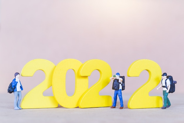 Mochilero de personas en miniatura de pie sobre el número de madera 2022, feliz año nuevo concepto