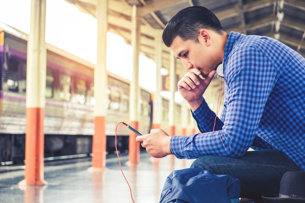 Mochilero turístico que usa el teléfono móvil para viajar en la estación de tren