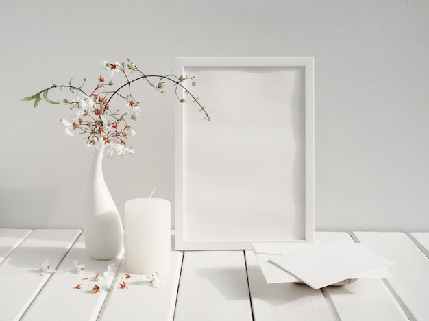 Foto mock-se cartão de convite branco, moldura de pôster, vela e belas flores clerodendron nodding em vaso erâmico na mesa de madeira interior de quarto branco, cartão em tom suave natureza morta