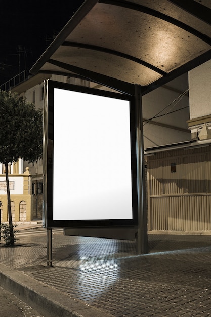 Foto mock-se da caixa de luz vertical branca em branco em uma parada de ônibus em uma cidade à noite