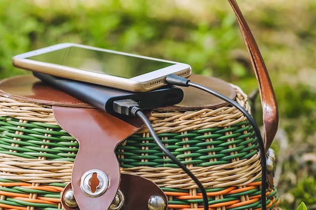 Mock-se de um smartphone com carregamento de Power Bank em uma cesta na floresta. Conceito sobre o tema da recreação ao ar livre.