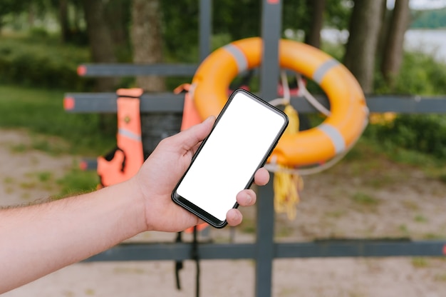 Foto mock-se de um smartphone na mão de um cara. no contexto de uma bóia salva-vidas e um colete.