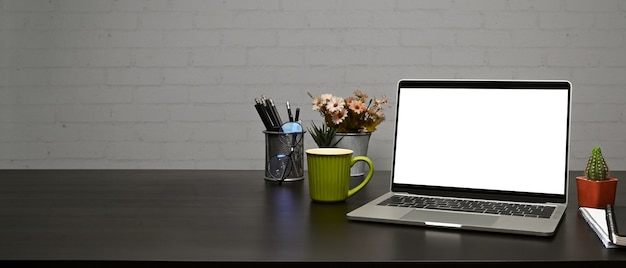 Mock-se laptop, xícara de café e porta-lápis na mesa de madeira com parede de tijolos.