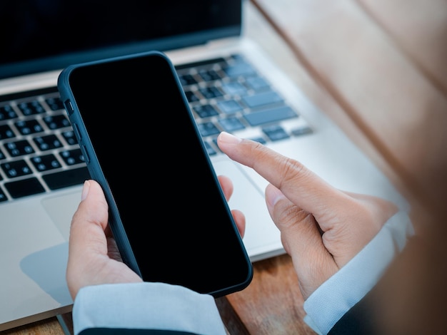Mock-up-Bildschirm auf schwarzem Smartphone in der Hand einer Geschäftsperson, die in der Nähe des Laptop-Computers hält Zeigen Sie mit dem Finger auf die Anwendung auf dem Mobiltelefon Investitions- und Geschäftstechnologiekonzepte