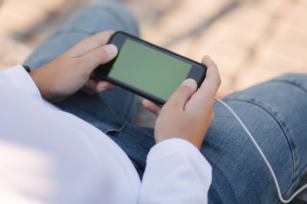 Mock up de boy play games en el teléfono inteligente Bahía sostenga el teléfono horizontalmente Pantalla verde Carga por banco de energía