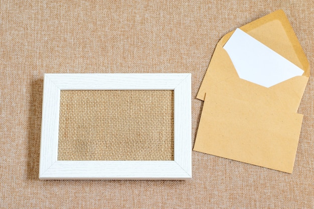 Mock up de mesa com moldura de madeira branca, envelopes em tecido de estopa texturizado