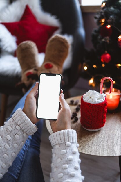 Mock-up des Smartphones in der Hand des Mädchens auf dem Hintergrund des Weihnachtsbaums mit festlicher Dekoration