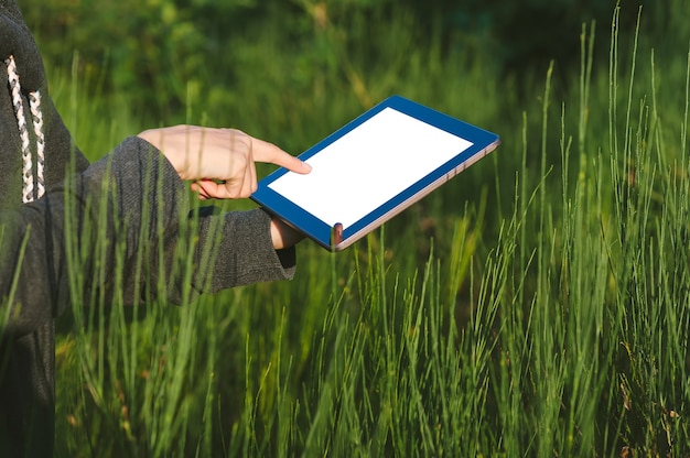 Mock-up eines Tablets mit einem Finger in der Nähe des Bildschirms auf dem Hintergrund einer schönen grünen Natur.