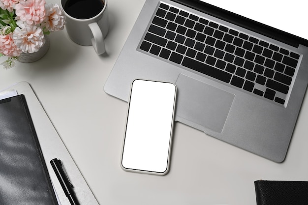 Foto mock-up smartphone, laptop-computer und kaffeetasse auf weißem schreibtisch.