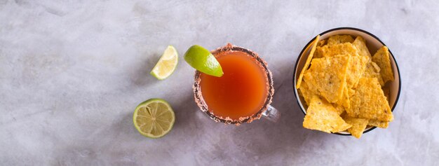 Mocktail de Michelagua com suco de tomate e suco de limão em um copo e banner da web de vista superior de nachos