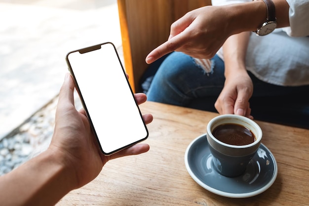 Mockup-Bild einer Frau, die auf ein weißes Mobiltelefon mit einem leeren schwarzen Desktop-Bildschirm in der Hand eines Mannes zeigt