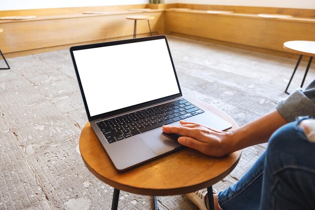 Mockup-Bild einer Frau, die das Touchpad eines Laptops mit einem leeren weißen Desktop-Bildschirm auf dem Tisch verwendet und berührt