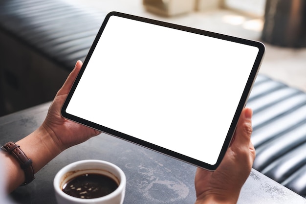 Mockup-Bild einer Frau, die ein digitales Tablet mit einem leeren weißen Desktop-Bildschirm im Café hält