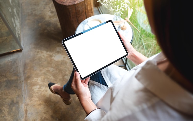 Mockup-Bild einer Frau, die ein digitales Tablet mit einem leeren weißen Desktop-Bildschirm im Café hält