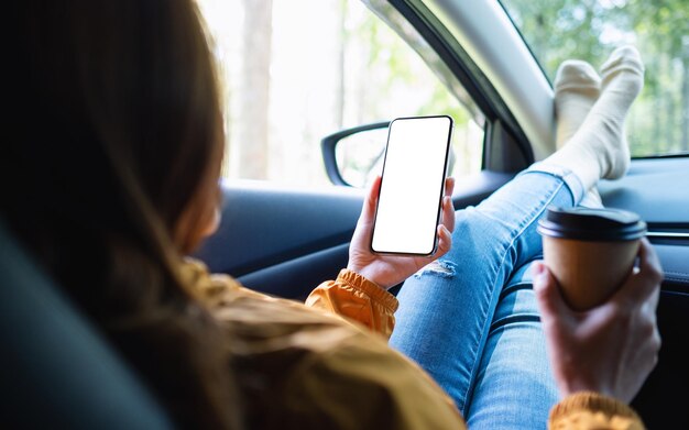 Mockup-Bild einer Frau, die ein Handy mit leerem Bildschirm hält und benutzt, während sie Kaffee trinkt und im Auto liegt