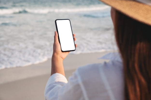 Mockup-Bild einer Frau, die ein Handy mit leerem Desktop-Bildschirm am Strand hält