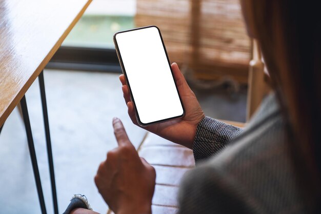 Mockup-Bild einer Frau, die ein Mobiltelefon mit einem leeren weißen Desktop-Bildschirm hält und mit dem Finger darauf zeigt