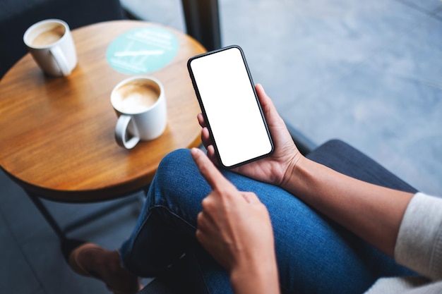 Mockup-Bild einer Frau, die ein Mobiltelefon mit einem leeren weißen Desktop-Bildschirm im Café hält und benutzt