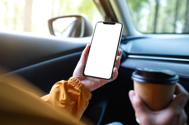 Mockup-Bild einer Frau, die ein Mobiltelefon mit leerem Bildschirm hält und benutzt, während sie im Auto Kaffee trinkt