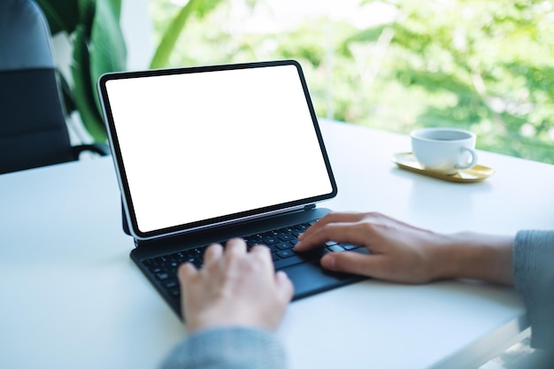 Mockup-Bild einer Frau, die eine Tablet-Tastatur mit einem leeren weißen Desktop-Bildschirm als Computer im Büro verwendet und tippt