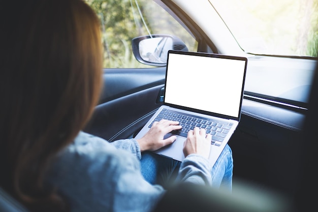 Mockup-Bild einer Frau, die einen Laptop-Computer mit leerem Desktop-Bildschirm im Auto verwendet und darauf tippt