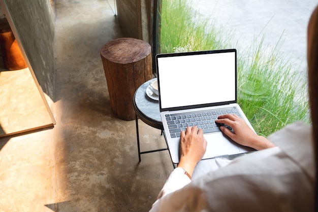 Mockup-Bild einer Frau, die einen Laptop-Computer mit leerem weißem Desktop-Bildschirm im Café verwendet und tippt