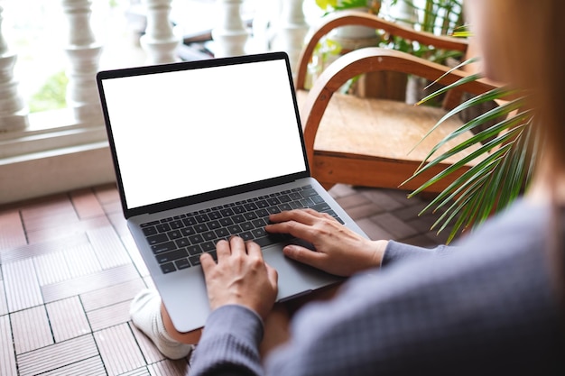 Mockup-Bild einer Frau, die einen Laptop mit einem leeren weißen Desktop-Bildschirm verwendet und daran arbeitet, während sie zu Hause auf dem Balkon sitzt