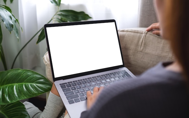 Mockup-Bild einer Frau, die einen Laptop mit leerem Desktop-Bildschirm verwendet und daran arbeitet, während sie zu Hause auf dem Sofa sitzt