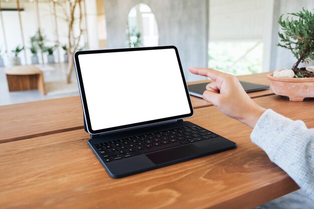 Mockup-Bild einer Frau, die einen Tablet-PC mit einem leeren weißen Desktop-Bildschirm als Computer-PC auf einem Holztisch verwendet und mit dem Finger darauf zeigt