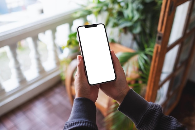 Mockup-Bild einer Frau, die zu Hause auf dem Balkon ein Handy mit leerem Desktop-Bildschirm hält