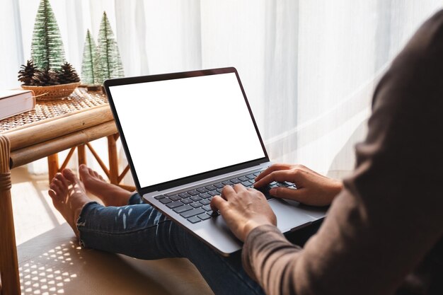 Mockup-Bild einer Frau, die zu Hause auf einem Laptop-Computer mit leerem weißen Bildschirm arbeitet und tippt