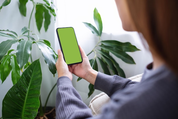 Mockup-Bild einer Frau, die zu Hause ein Mobiltelefon mit leerem Desktop-Bildschirm hält